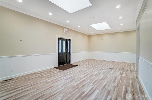 empty room with crown molding, light hardwood / wood-style flooring, and a skylight