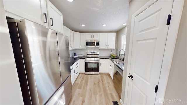 kitchen with light wood-type flooring, stainless steel appliances, white cabinetry, and tasteful backsplash