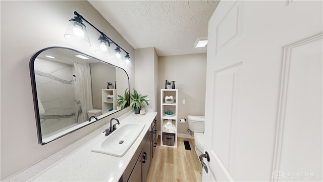 bathroom with toilet, a textured ceiling, wood-type flooring, a shower, and vanity