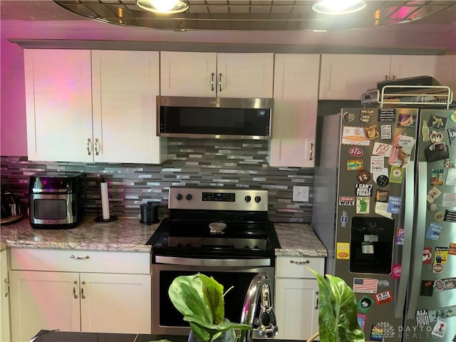 kitchen with white cabinets, stainless steel appliances, light stone countertops, and decorative backsplash