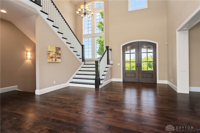 foyer with a towering ceiling, french doors, an inviting chandelier, and dark hardwood / wood-style flooring