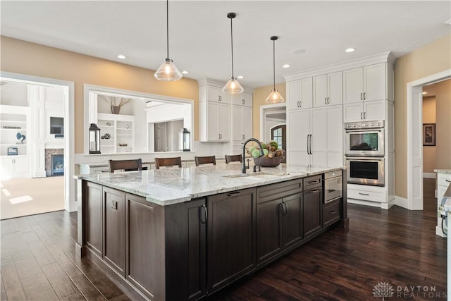 kitchen with white cabinets, dark wood-type flooring, double oven, sink, and hanging light fixtures