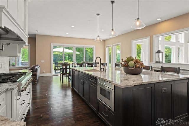 kitchen with appliances with stainless steel finishes, white cabinetry, sink, pendant lighting, and an island with sink