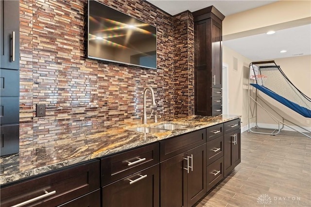 bar featuring light stone countertops, sink, dark brown cabinetry, and decorative backsplash