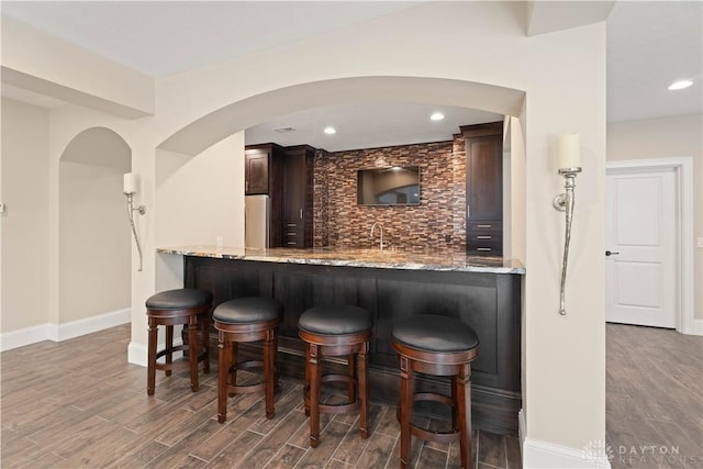 bar featuring decorative backsplash, light stone countertops, sink, and dark brown cabinets