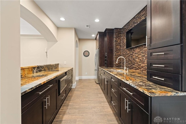 kitchen with stone countertops, sink, backsplash, light wood-type flooring, and stainless steel appliances