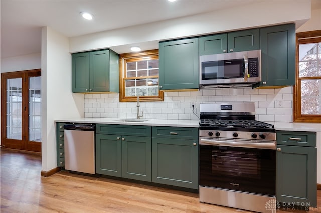 kitchen with sink, appliances with stainless steel finishes, green cabinets, light hardwood / wood-style floors, and backsplash