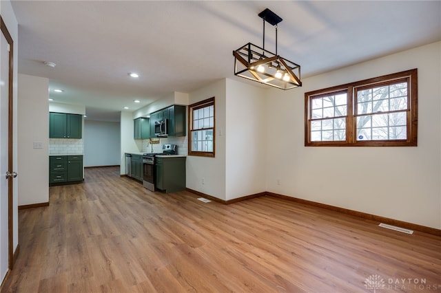 interior space with pendant lighting, green cabinets, appliances with stainless steel finishes, backsplash, and light wood-type flooring