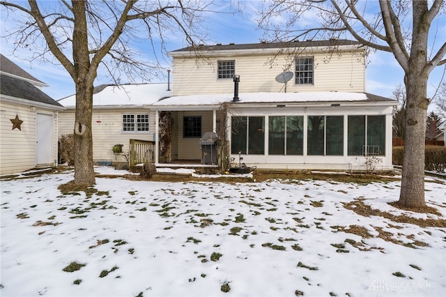 snow covered back of property featuring a sunroom