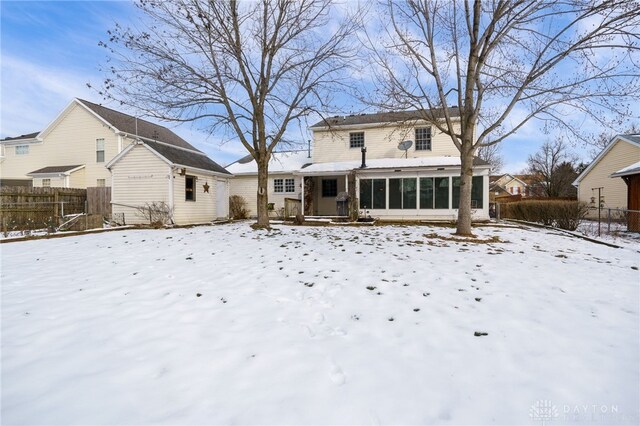 snow covered rear of property with a sunroom