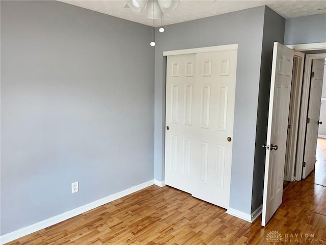 unfurnished bedroom featuring a closet, light wood-style flooring, and baseboards