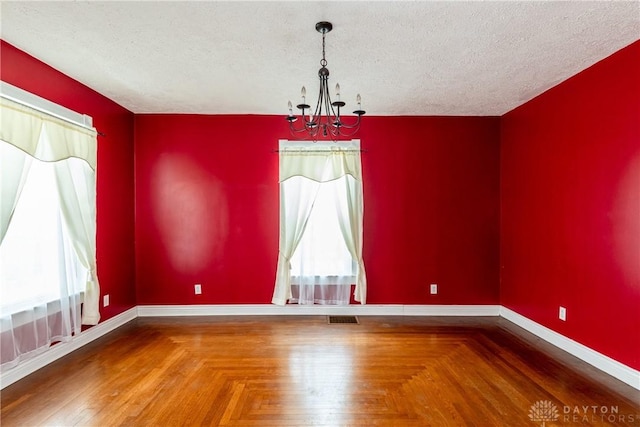 empty room featuring parquet flooring, a textured ceiling, and a notable chandelier