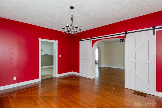 unfurnished dining area featuring ceiling fan with notable chandelier, a textured ceiling, and a barn door