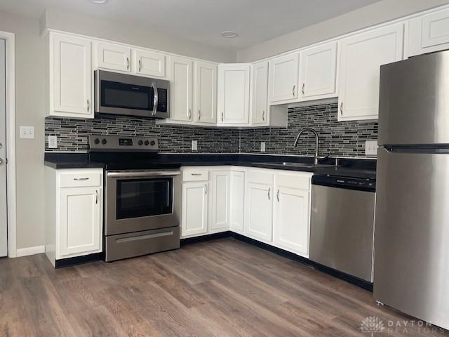 kitchen featuring tasteful backsplash, white cabinetry, sink, dark wood-type flooring, and stainless steel appliances