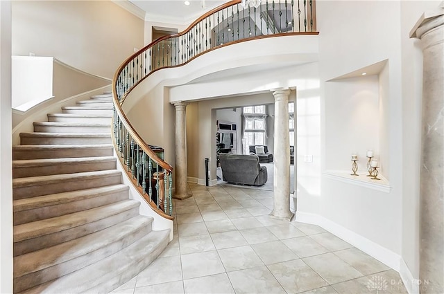 tiled foyer with crown molding, decorative columns, and a high ceiling