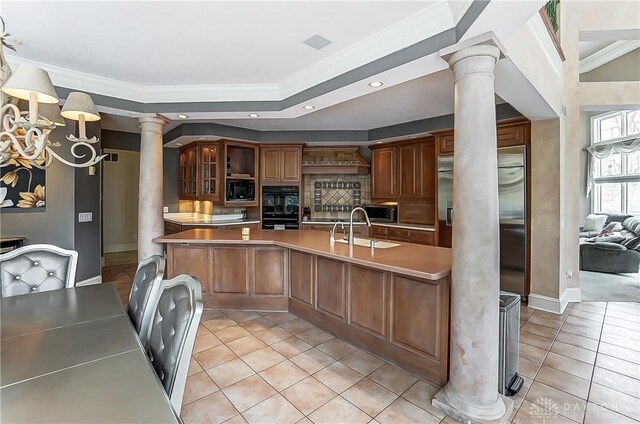 kitchen with ornate columns, black appliances, sink, kitchen peninsula, and crown molding