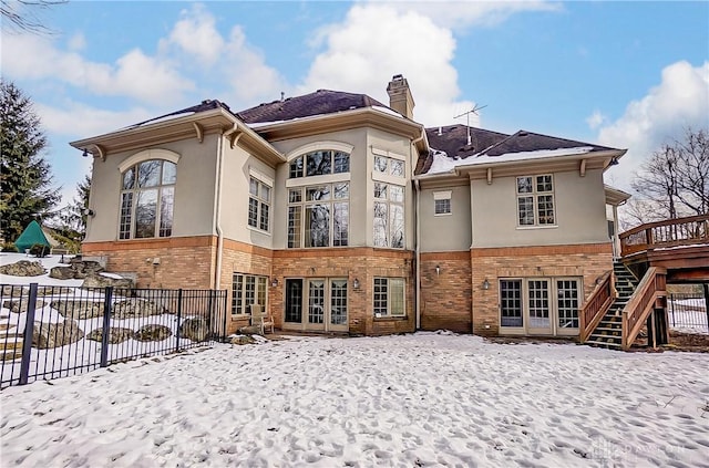 snow covered rear of property with a deck and french doors