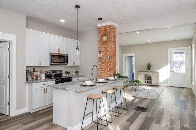 kitchen with light stone countertops, appliances with stainless steel finishes, white cabinetry, sink, and hanging light fixtures