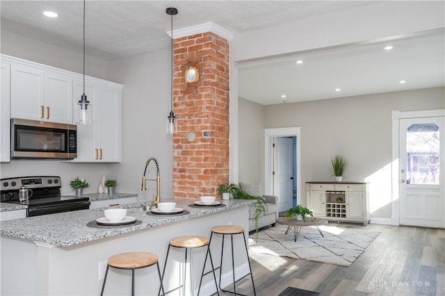 kitchen featuring pendant lighting, appliances with stainless steel finishes, white cabinetry, light stone counters, and a breakfast bar area