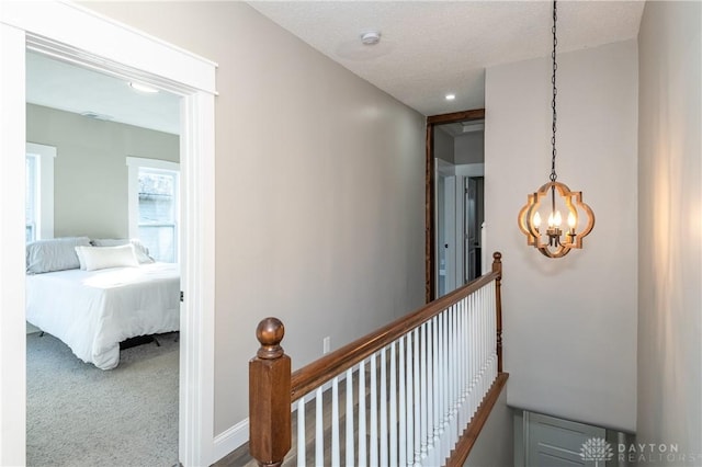 corridor with a textured ceiling, carpet flooring, and a notable chandelier