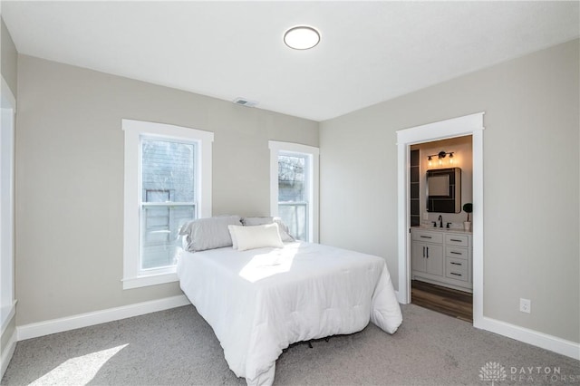 carpeted bedroom featuring multiple windows, connected bathroom, and sink