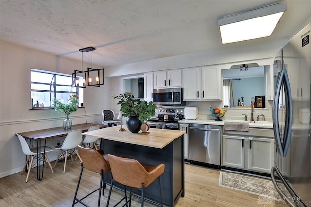 kitchen with light hardwood / wood-style floors, white cabinetry, hanging light fixtures, sink, and stainless steel appliances