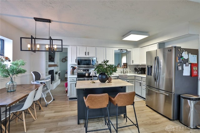 kitchen with a textured ceiling, white cabinets, a center island, decorative light fixtures, and stainless steel appliances