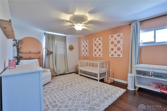 bedroom featuring a crib, dark wood-type flooring, and ceiling fan