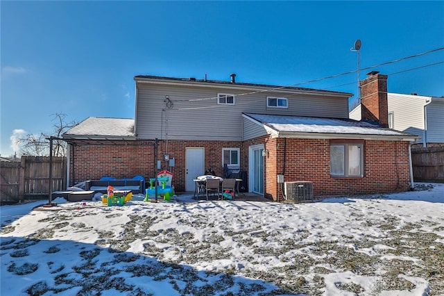 snow covered rear of property featuring an outdoor living space and central AC unit