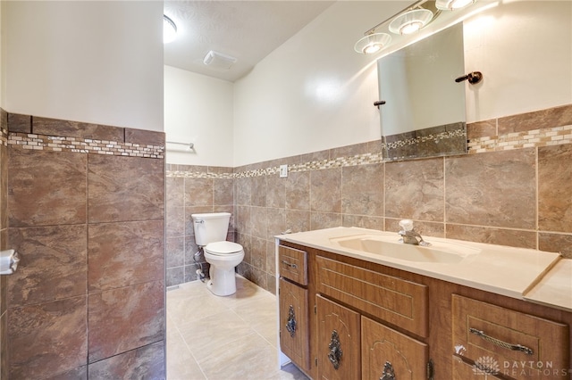 bathroom featuring toilet, vanity, tile patterned floors, and tile walls