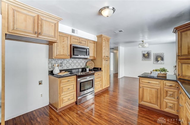 kitchen with backsplash, dark stone counters, appliances with stainless steel finishes, and dark wood-type flooring