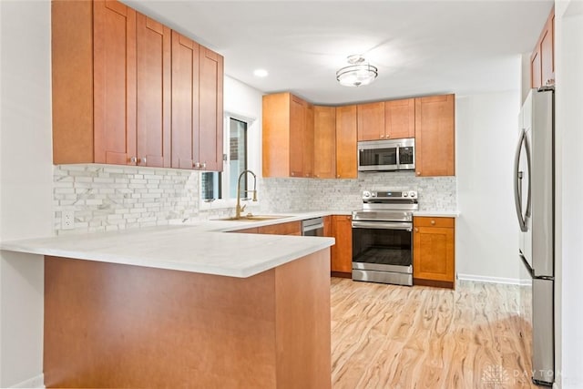 kitchen with tasteful backsplash, sink, kitchen peninsula, stainless steel appliances, and light hardwood / wood-style flooring