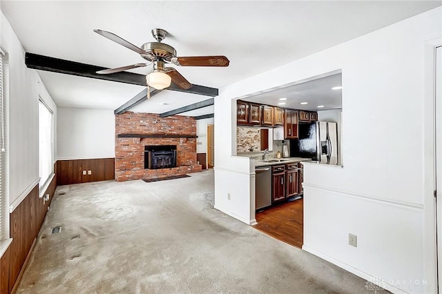 unfurnished living room with sink, ceiling fan, wooden walls, dark carpet, and beamed ceiling