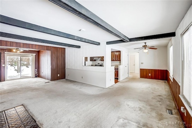 unfurnished living room featuring ceiling fan, beam ceiling, carpet, and wood walls