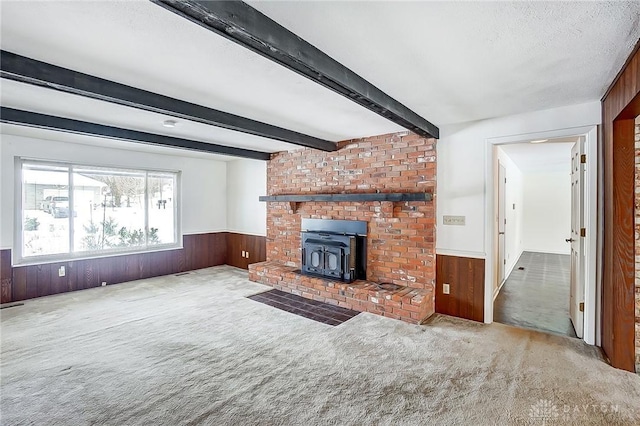 unfurnished living room featuring beamed ceiling, a wood stove, light carpet, and wood walls