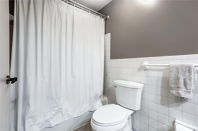 bathroom featuring toilet, shower / bathtub combination with curtain, and tile walls