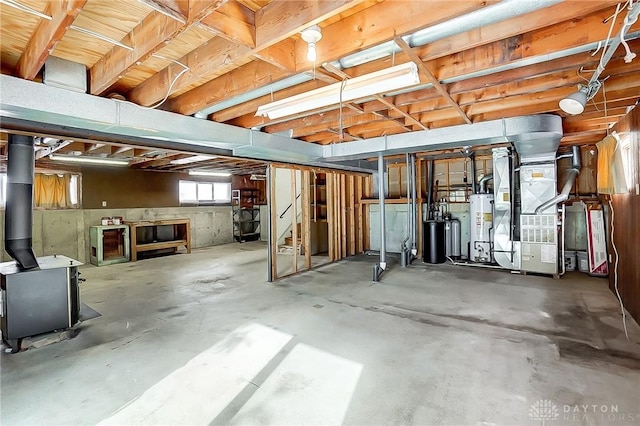 basement with gas water heater, a wood stove, and heating unit