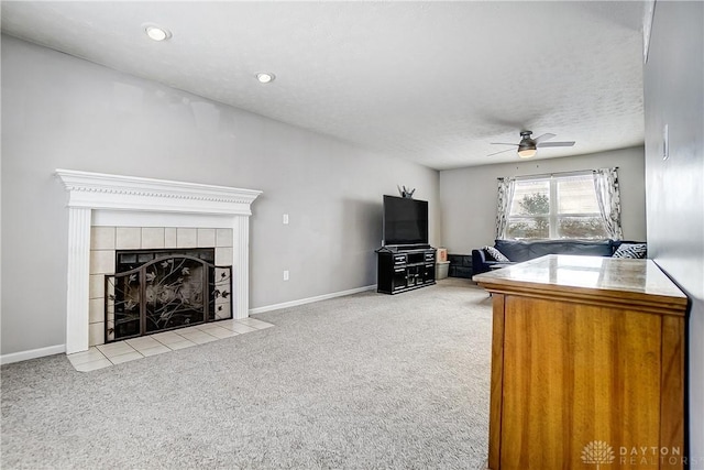 living room with light carpet, ceiling fan, a tile fireplace, and a textured ceiling