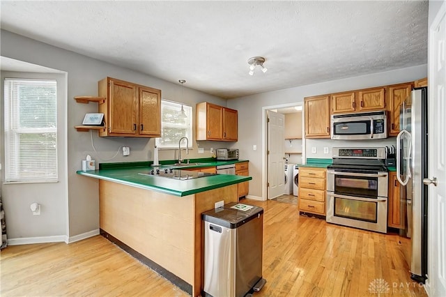 kitchen featuring appliances with stainless steel finishes, kitchen peninsula, independent washer and dryer, light hardwood / wood-style floors, and a textured ceiling