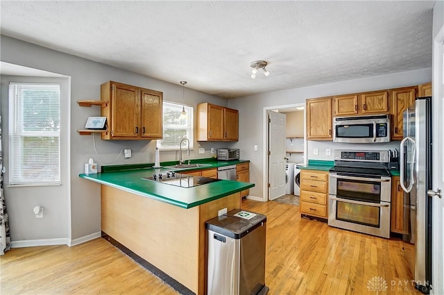 kitchen with sink, light hardwood / wood-style flooring, a textured ceiling, appliances with stainless steel finishes, and kitchen peninsula