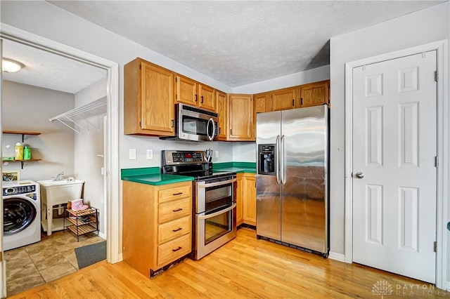 kitchen with sink, light hardwood / wood-style flooring, appliances with stainless steel finishes, a textured ceiling, and washer / dryer