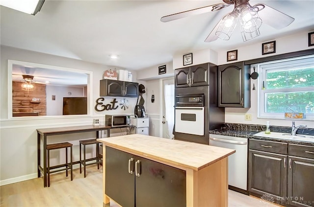 kitchen featuring ceiling fan, stainless steel appliances, a sink, dark brown cabinets, and light wood finished floors