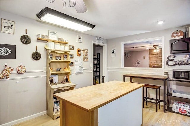 kitchen with light wood-style floors, butcher block countertops, stainless steel microwave, and a ceiling fan