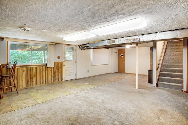 below grade area with stairway, light carpet, a textured ceiling, and wooden walls