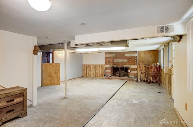 basement with light carpet, a brick fireplace, and wood walls