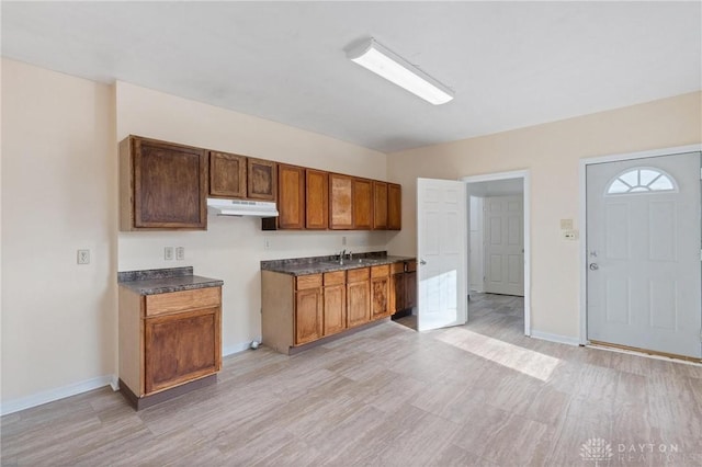 kitchen with baseboards, dark countertops, light wood-style flooring, and under cabinet range hood