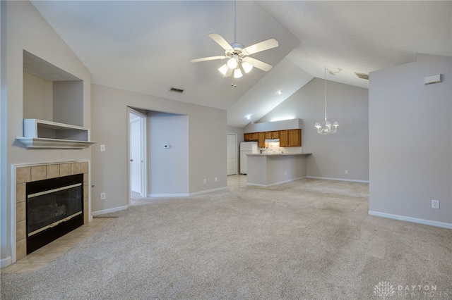 unfurnished living room with a tile fireplace, vaulted ceiling, ceiling fan with notable chandelier, and light colored carpet