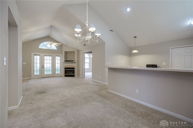 unfurnished living room with light carpet, ceiling fan with notable chandelier, a tile fireplace, and lofted ceiling