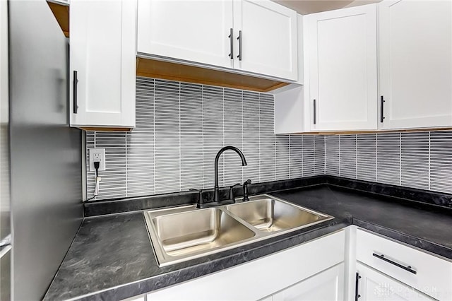 kitchen with white cabinetry, sink, decorative backsplash, and stainless steel refrigerator