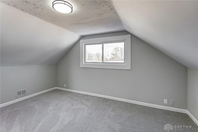 bonus room featuring light carpet, vaulted ceiling, and a textured ceiling